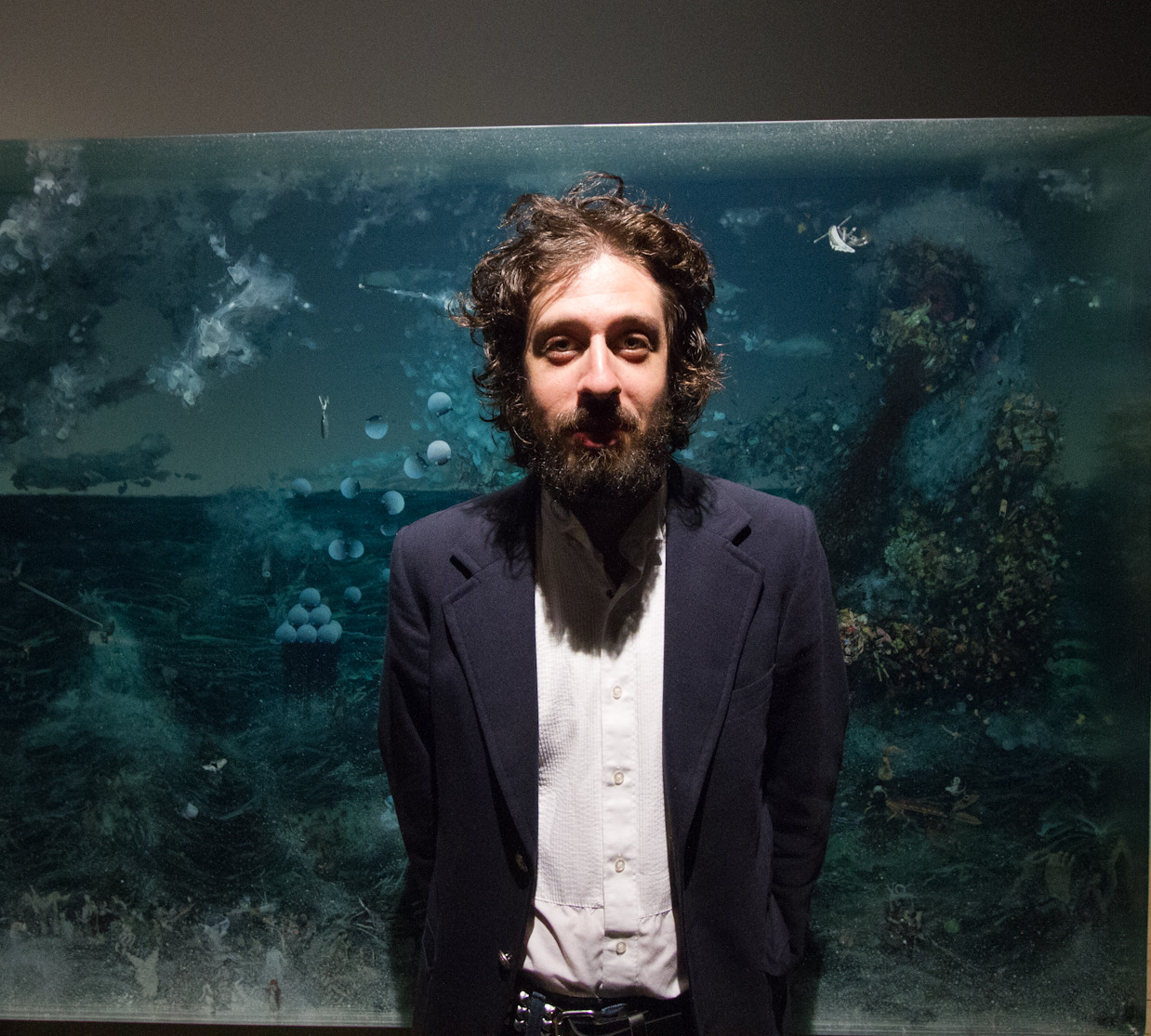 Dustin Yellin (b. 1975 Los Angeles, California)
Portrait from the artist&rsquo;s tumblr (Adam Green in front of Yellin&rsquo;s work)
Dustin Yellin is a renaissance man who, through many good fortunes, has come to develop quite a reputation in Redhook, Brooklyn. Besides having an incredible direction for his artistic works, Yellin also manages the real estate development for the warehouses he owns and has renovated into multiple nonprofit artist residency programs (including Kidd Yellin and a yet unnamed space on the corners of Pinoneer and King in Redhook) while also starting a new magazine called INTERCOURSE. Most famous for his layered drawings, Yellin works with both glass and resin to fixate found objects, drawings and oils into his three-dimensional works. Playing with natural and artificial lights, the layered pieces cast shadows on the walls in the gallery, creating unique atmospheres with each piece. When working with resin, the process involves a meticulous repetitive layering of the resin, allowing it to dry, drawing upon each layer, and repeat, until the large full work of art is created. Glass, as a medium, allows for the suspension of drawings between thin layers, similar to that of a microscopic slide. It is clear how the layers and parts develop the whole that is each piece. His works serve to simplify the complications but not erase them. For Yellin, it is that fragmentation of these complicated realities that allows viewers to comprehend the information, understanding the vast systems that may be discouragingly overwhelming otherwise.