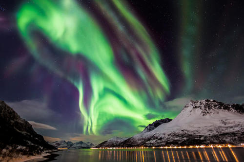 The spectacular Northern Lights unfold over a fjord, in Skjervøy, Troms, Norway.